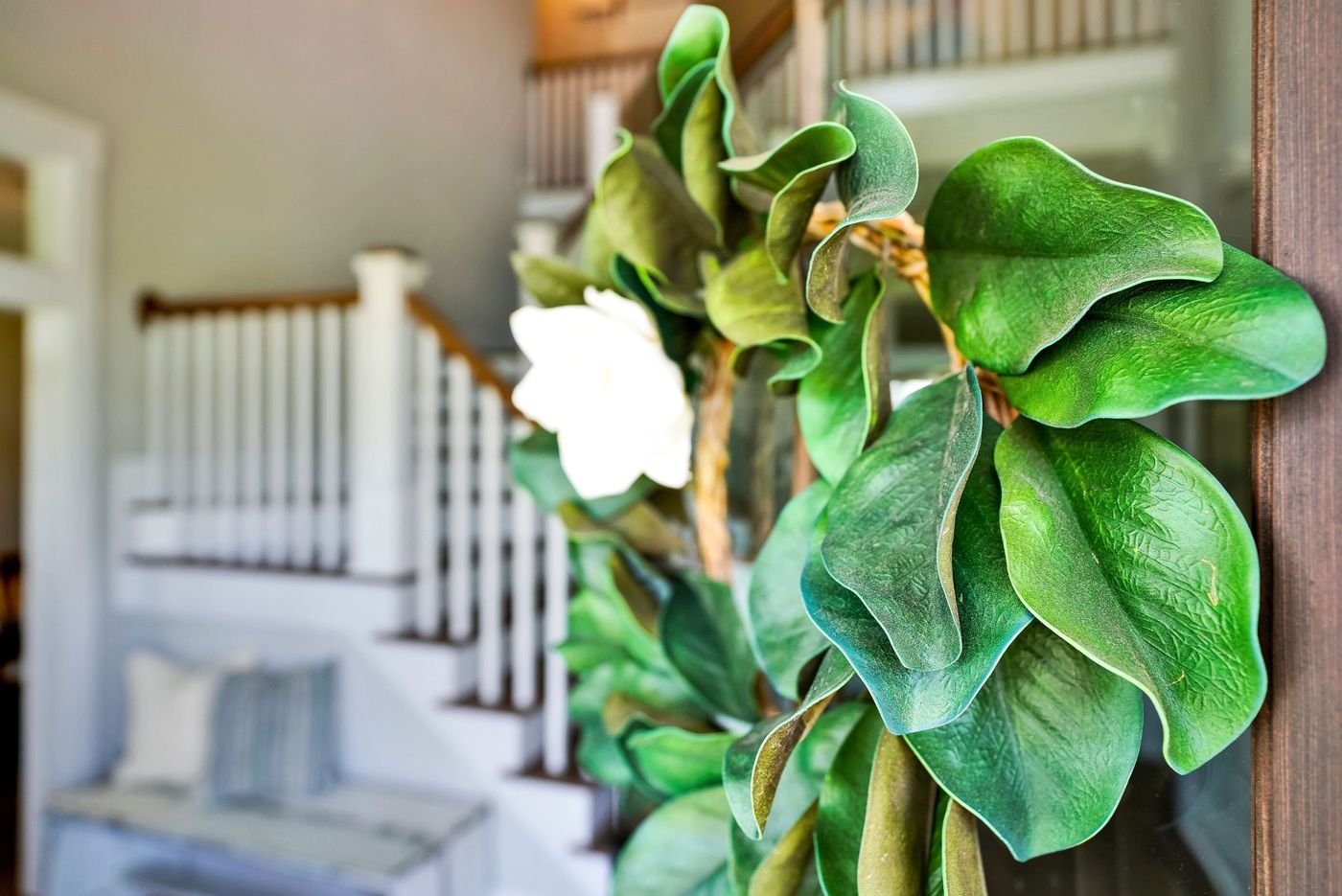 Magnolia wreath on a front door, with the entry and white staircase behind it