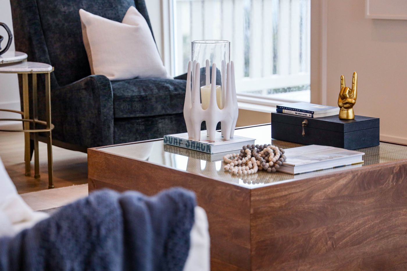 Staged living room with a wood coffee table, styled books and decor, and a navy velvet armchair